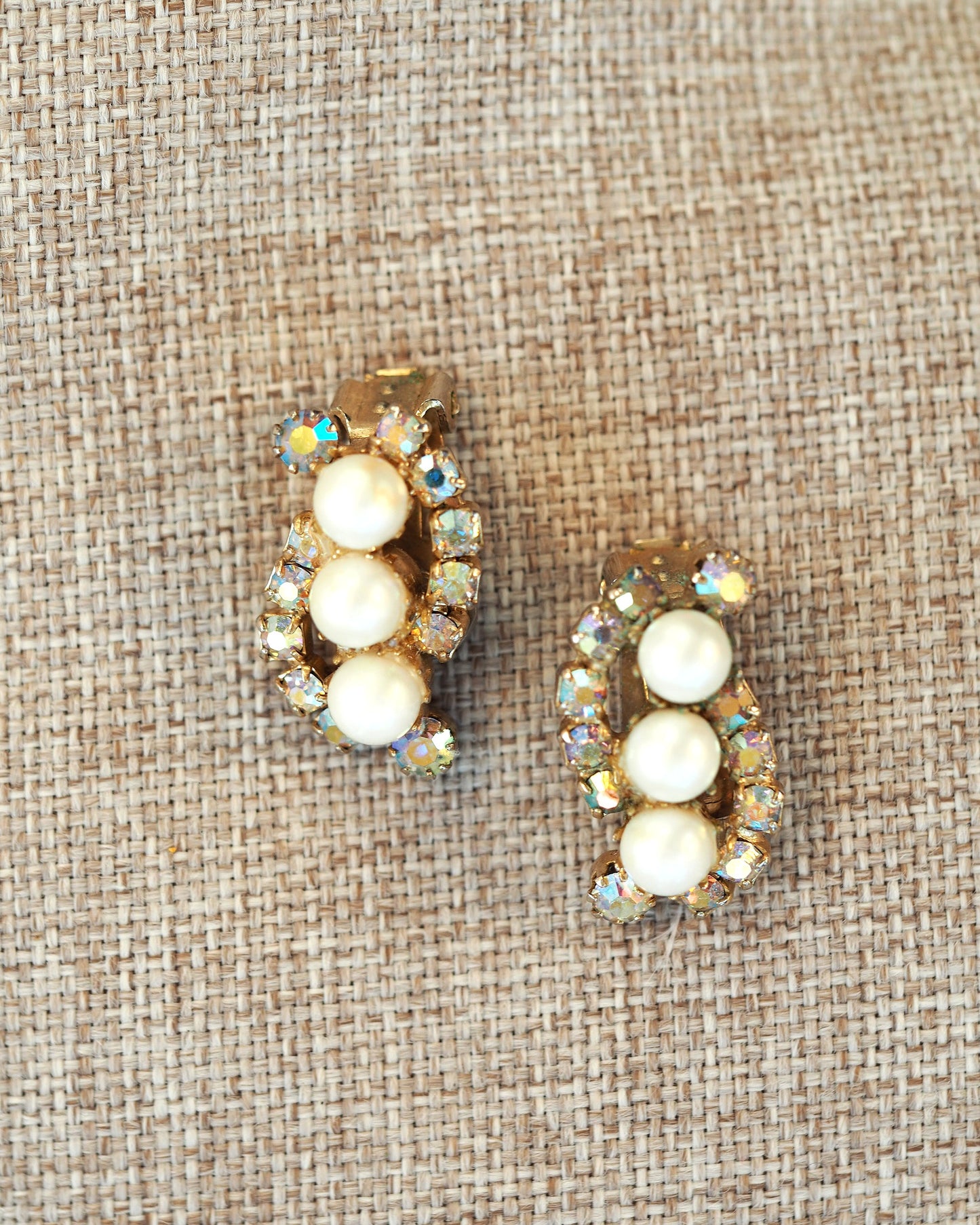 Hero shot of vintage pearl and AB rhinestone clip earrings in antique gold-tone finish on textured linen background