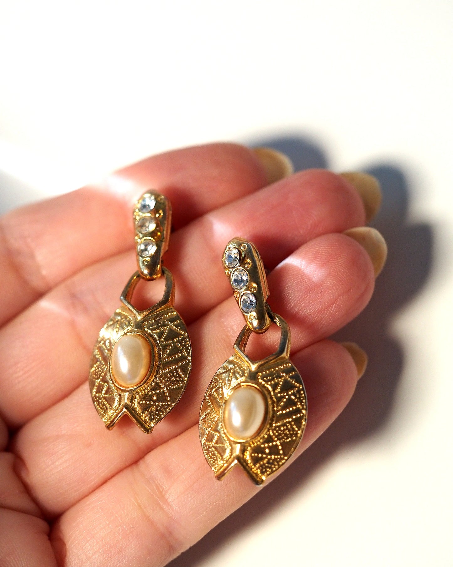 Gold-tone faux pearl rhinestone leaf drop earrings held in hand for scale, approximately 1.5 inches long