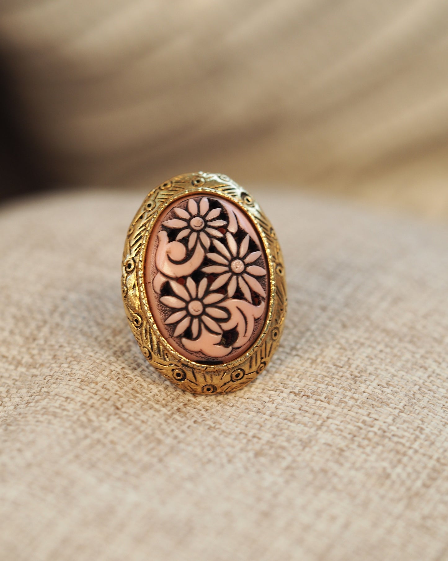 Gold-tone adjustable ring with pink carved daisy cabochon, front view on linen