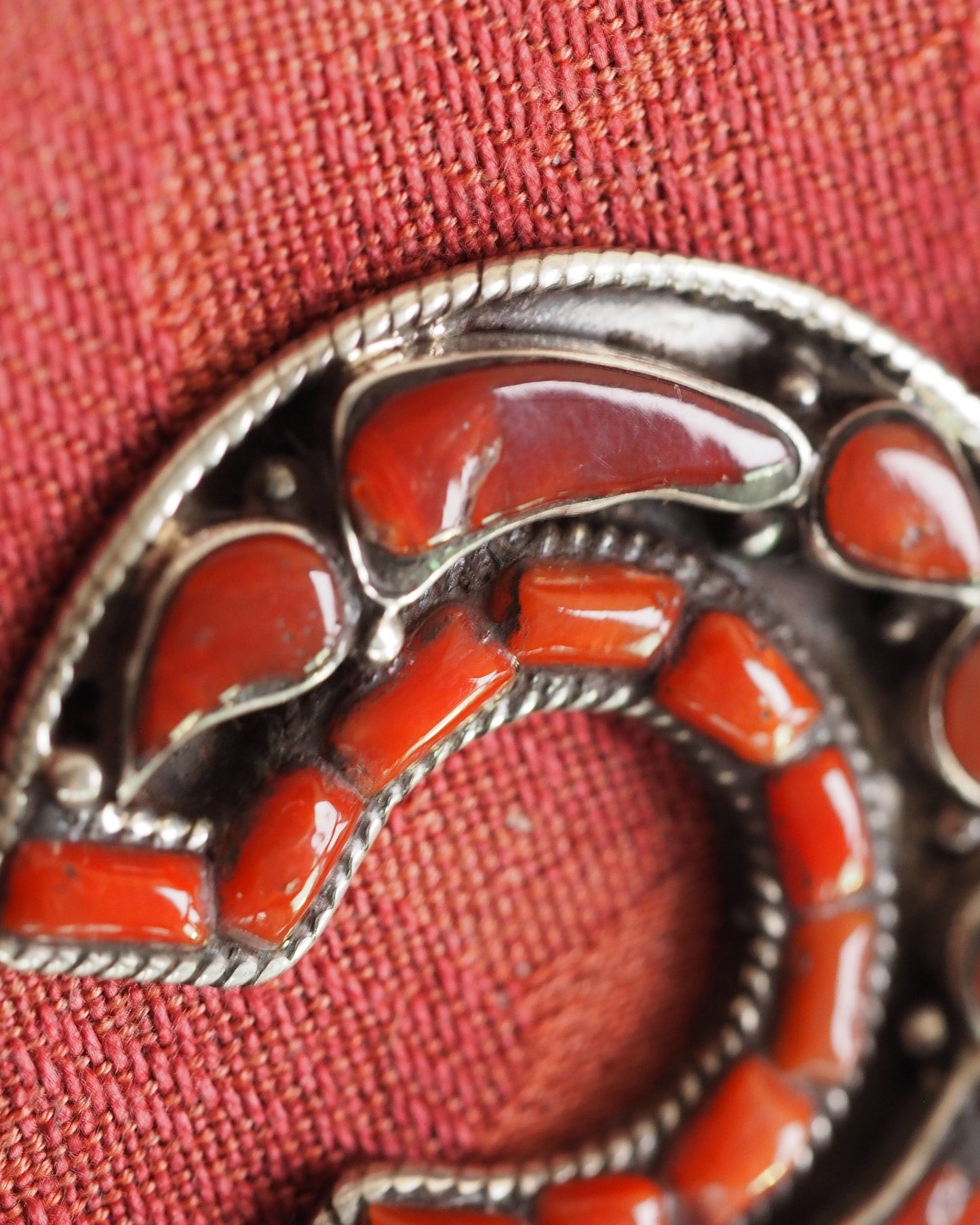 Close-up of red coral inlay in silver bezels, showing glossy cabochon surfaces and rope wire detail