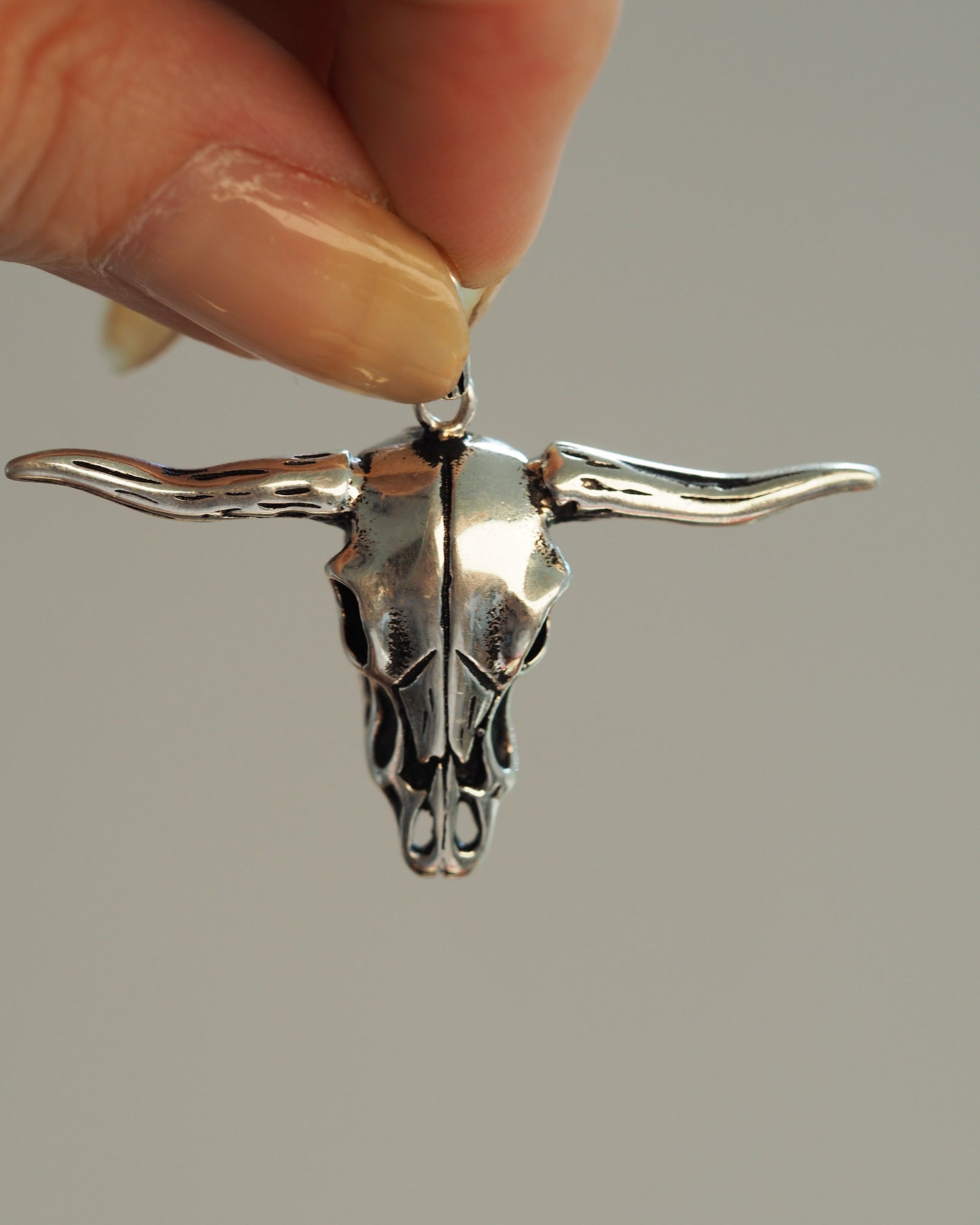Close-up front view of the longhorn skull pendant held between fingers, showing polished surfaces and dark recesses