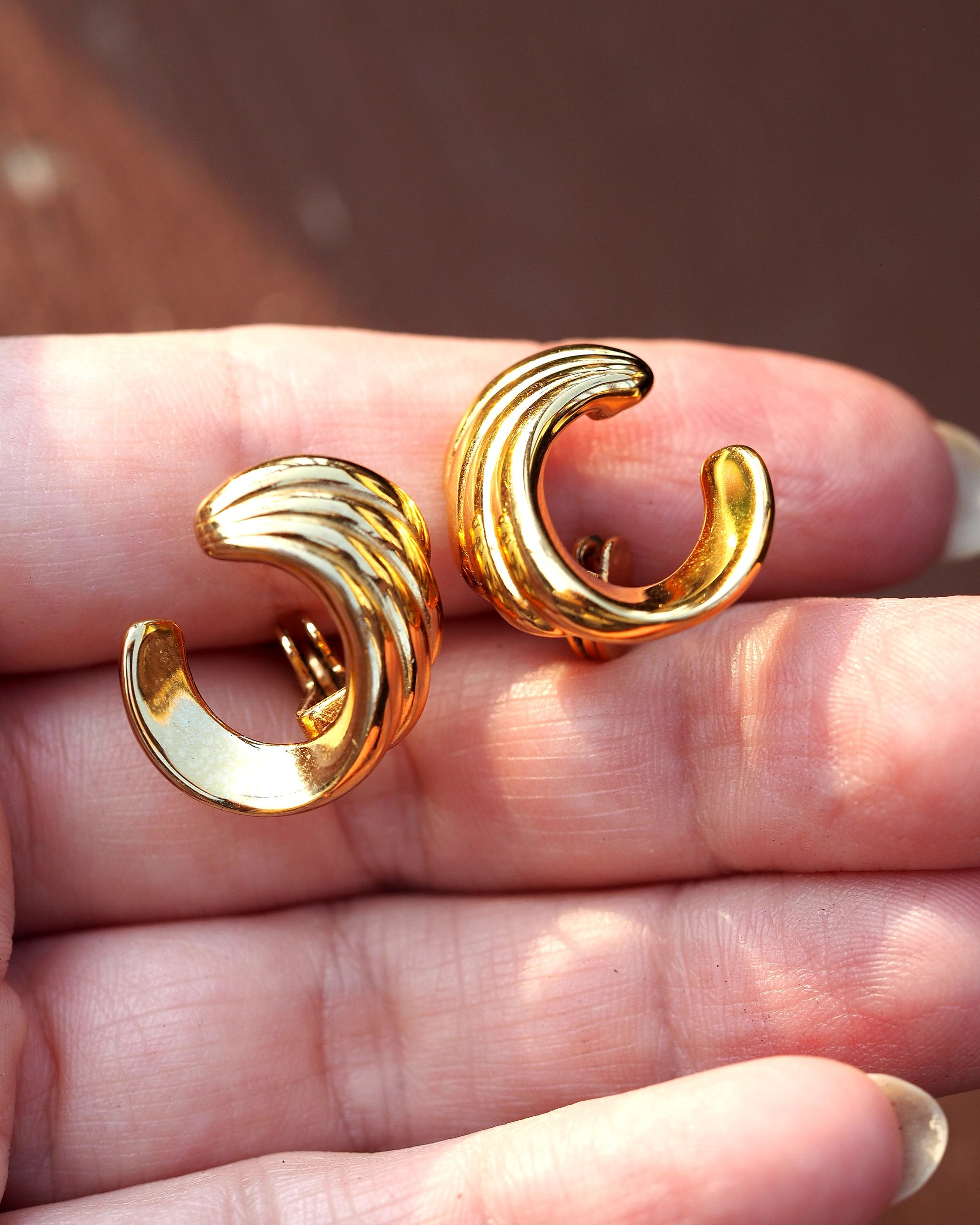 Monet swoosh clip earrings held on fingertips for scale, showing three-quarter-inch curved silhouette
