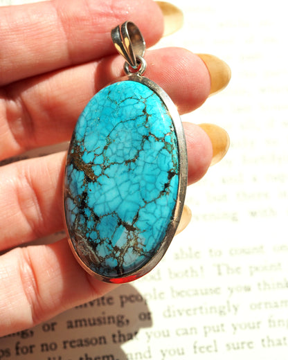 Sterling silver turquoise pendant held in hand, showing scale and oval shape with matrix detail