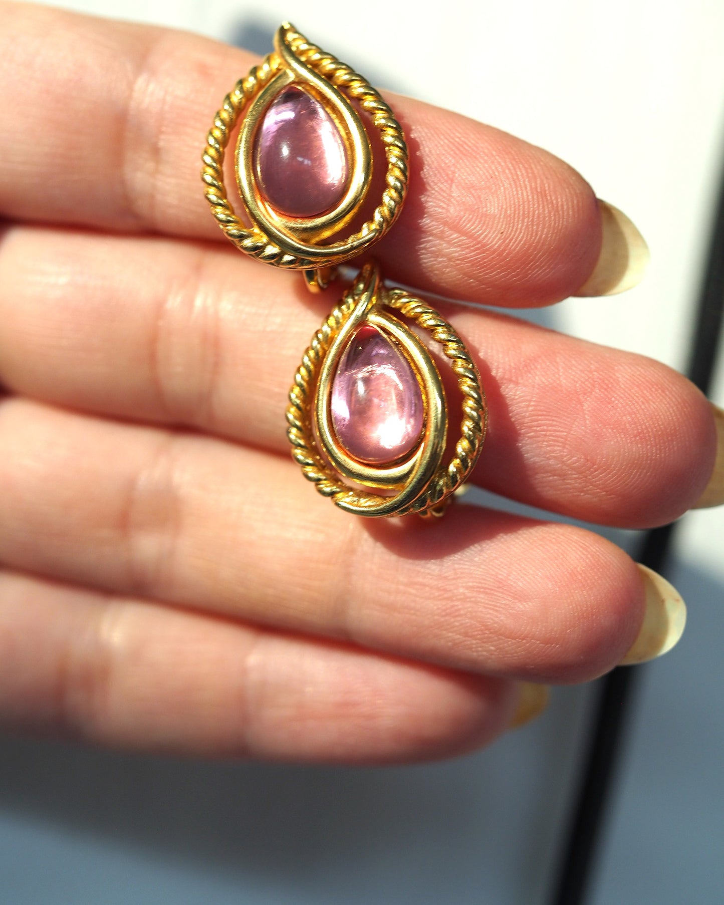 Both Trifari clip earrings held in fingers for scale, showing teardrop shape and pink cabochon depth