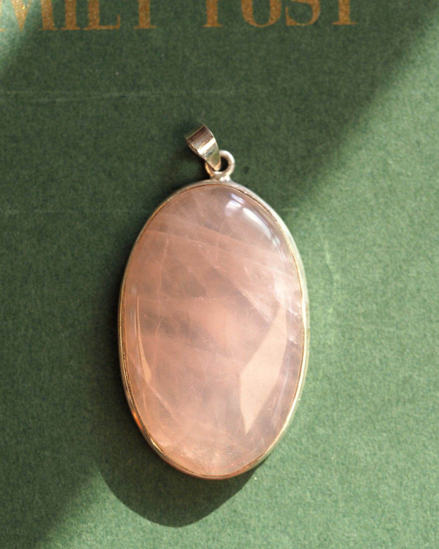 Sterling silver pendant with large faceted rose quartz oval, front view on green background