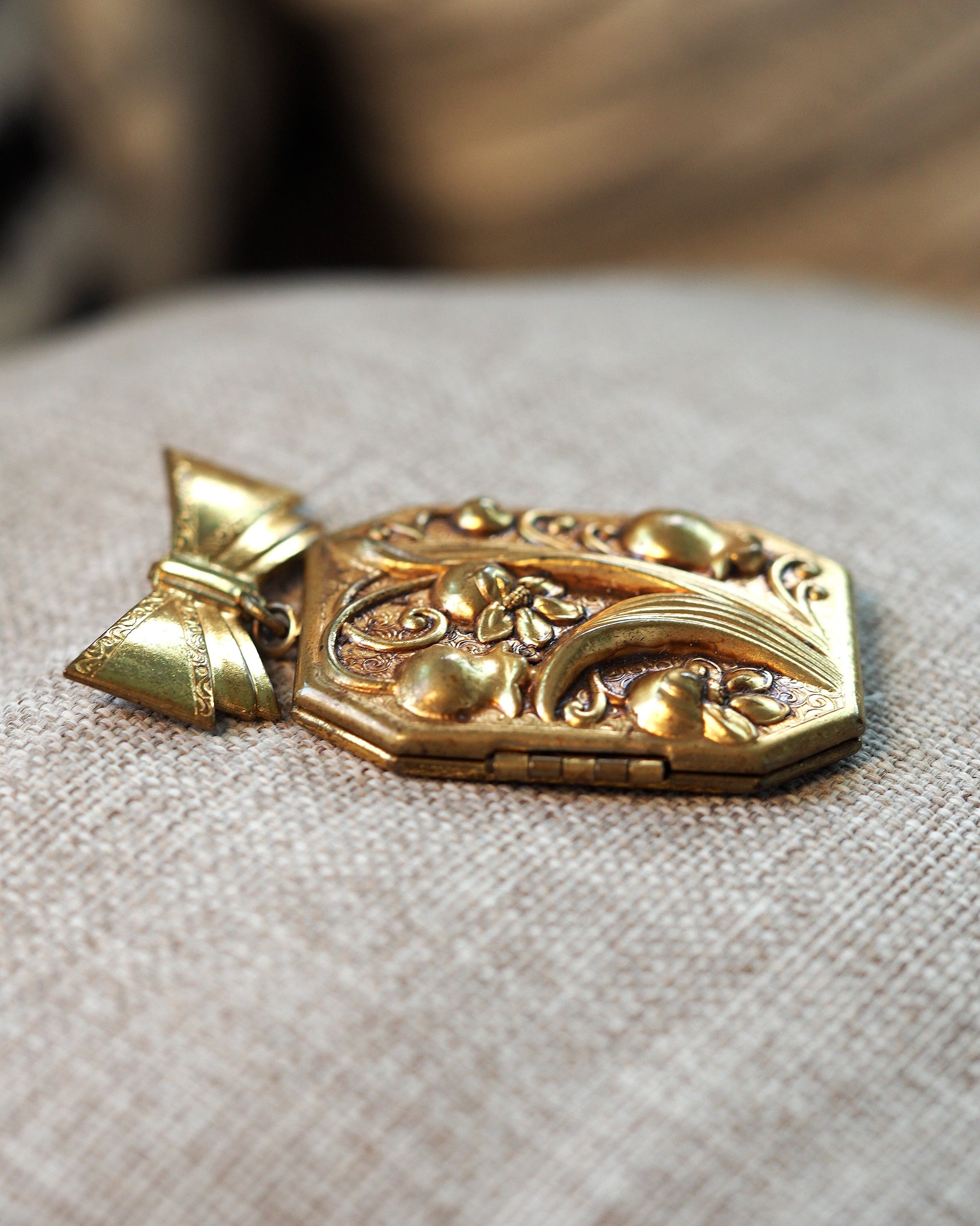 Side angle view of the gold-tone locket brooch showing dimensional relief and hinge detail