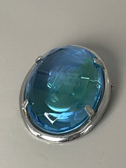 Blue glass cameo brooch, front view, showing faceted oval glass with intaglio-carved classical profile in silver-tone prong-set frame