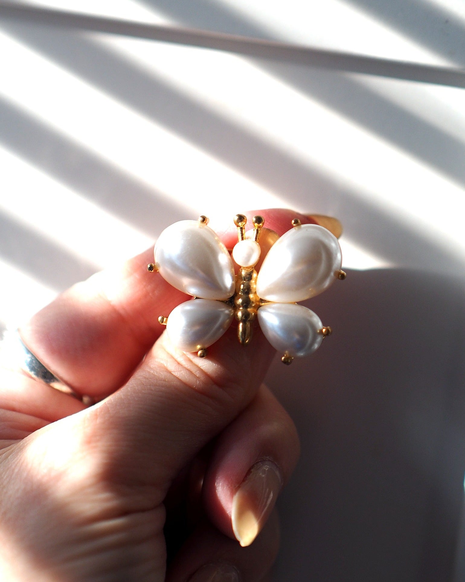 Faux-pearl butterfly brooch held between fingertips for scale, measuring just over an inch across