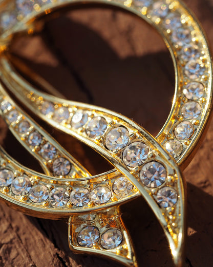 Close-up of prong-set clear rhinestones along the gold-tone ribbon curves, showing faceting and sparkle
