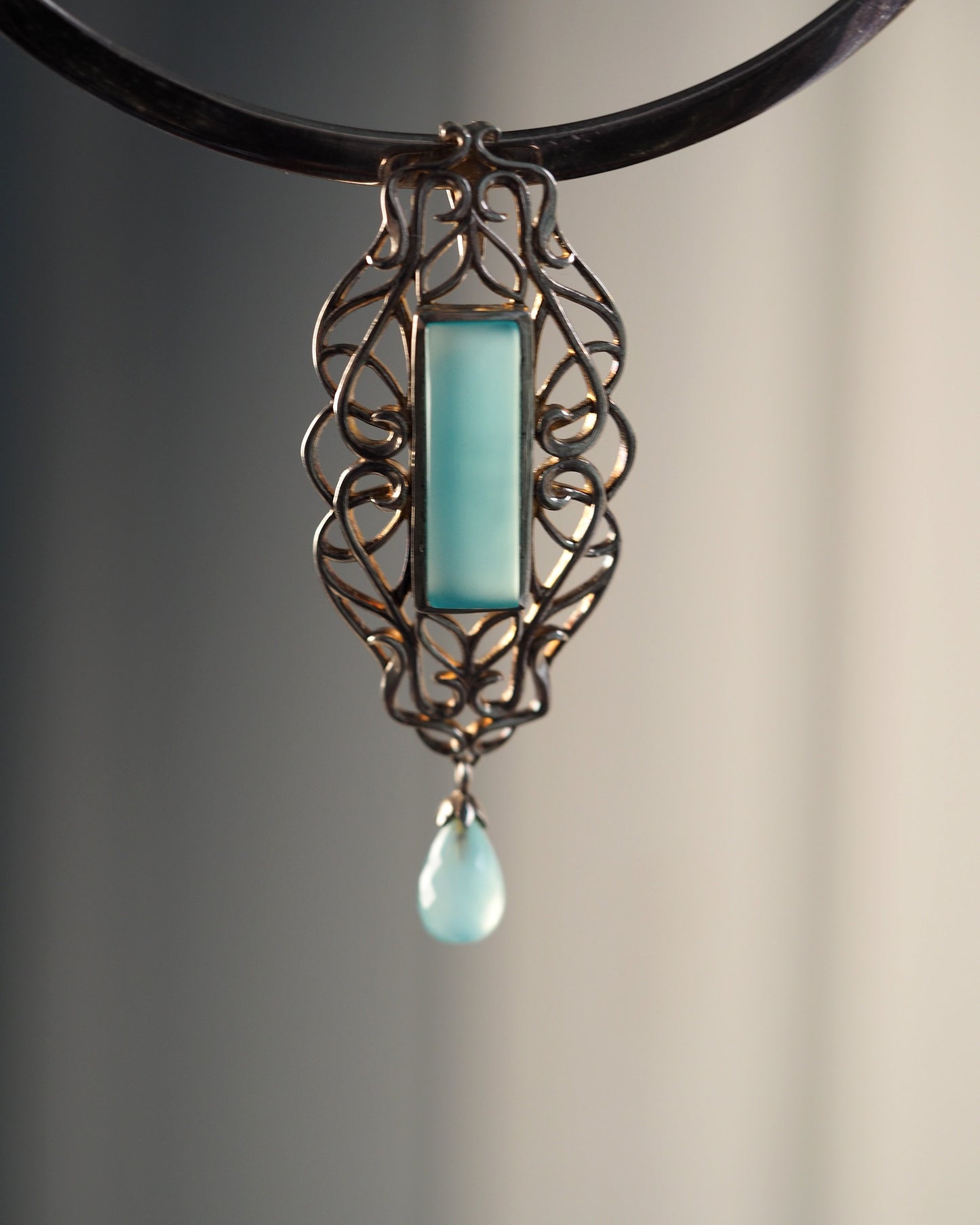 Sterling silver openwork Derewala pendant with rectangular aqua-blue chalcedony cabochon and teardrop dangle, front view on black cord