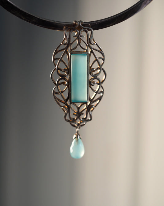 Sterling silver openwork Derewala pendant with rectangular aqua-blue chalcedony cabochon and teardrop dangle, front view on black cord