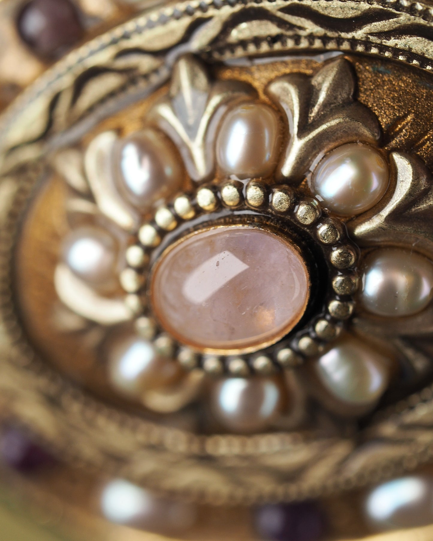 Close-up of rose-colored center cabochon in beaded bezel surrounded by pearl-like petals