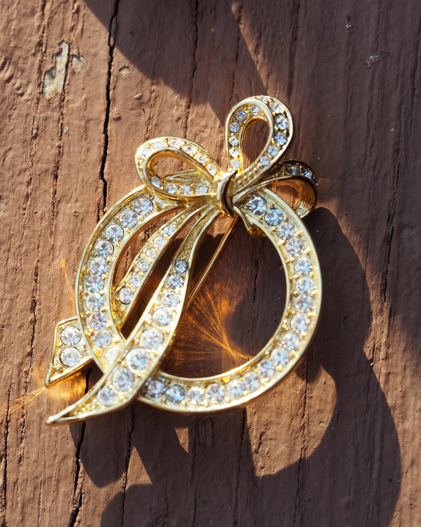 Nolan Miller rhinestone bow brooch in gold-tone, front view showing ribbon-and-bow silhouette with open circle center