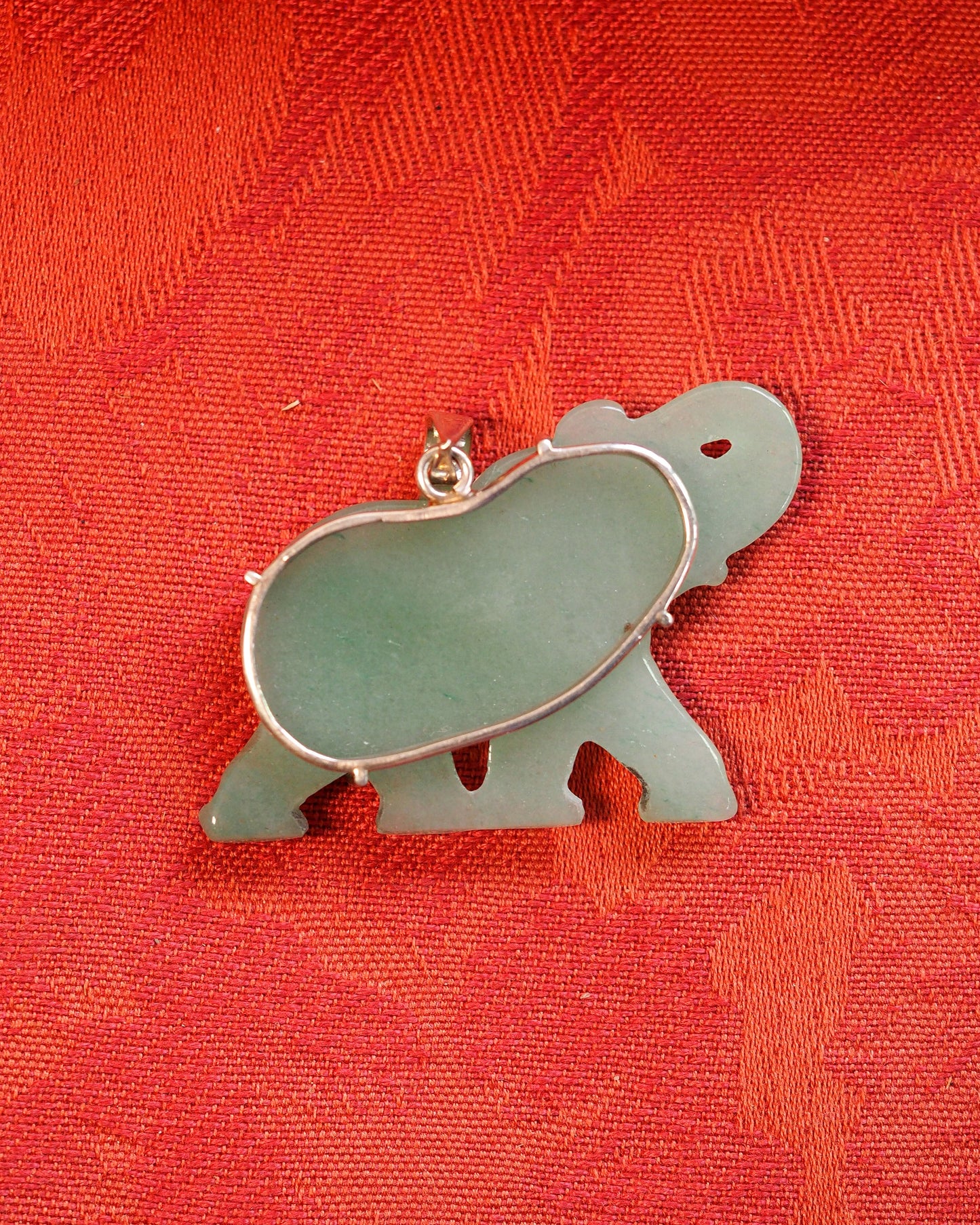 Back view of aventurine elephant pendant on red fabric, showing sterling silver prong mounts and natural color gradient in stone