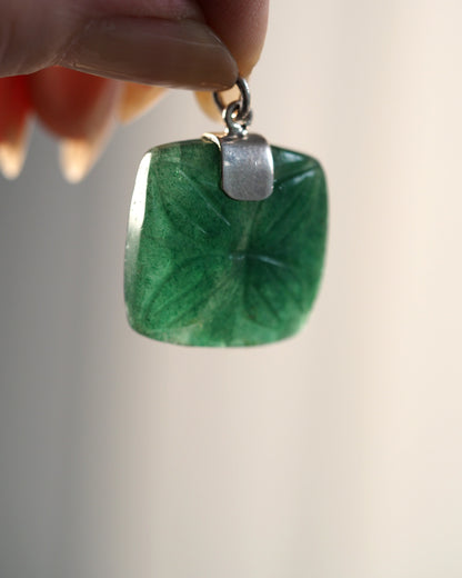 aventurine pendant held suspended to show light passing through the translucent green stone and carved pattern