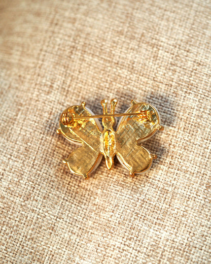 Reverse of faux-pearl butterfly brooch showing textured gold-tone back with crosshatch detail and straight pin-bar clasp