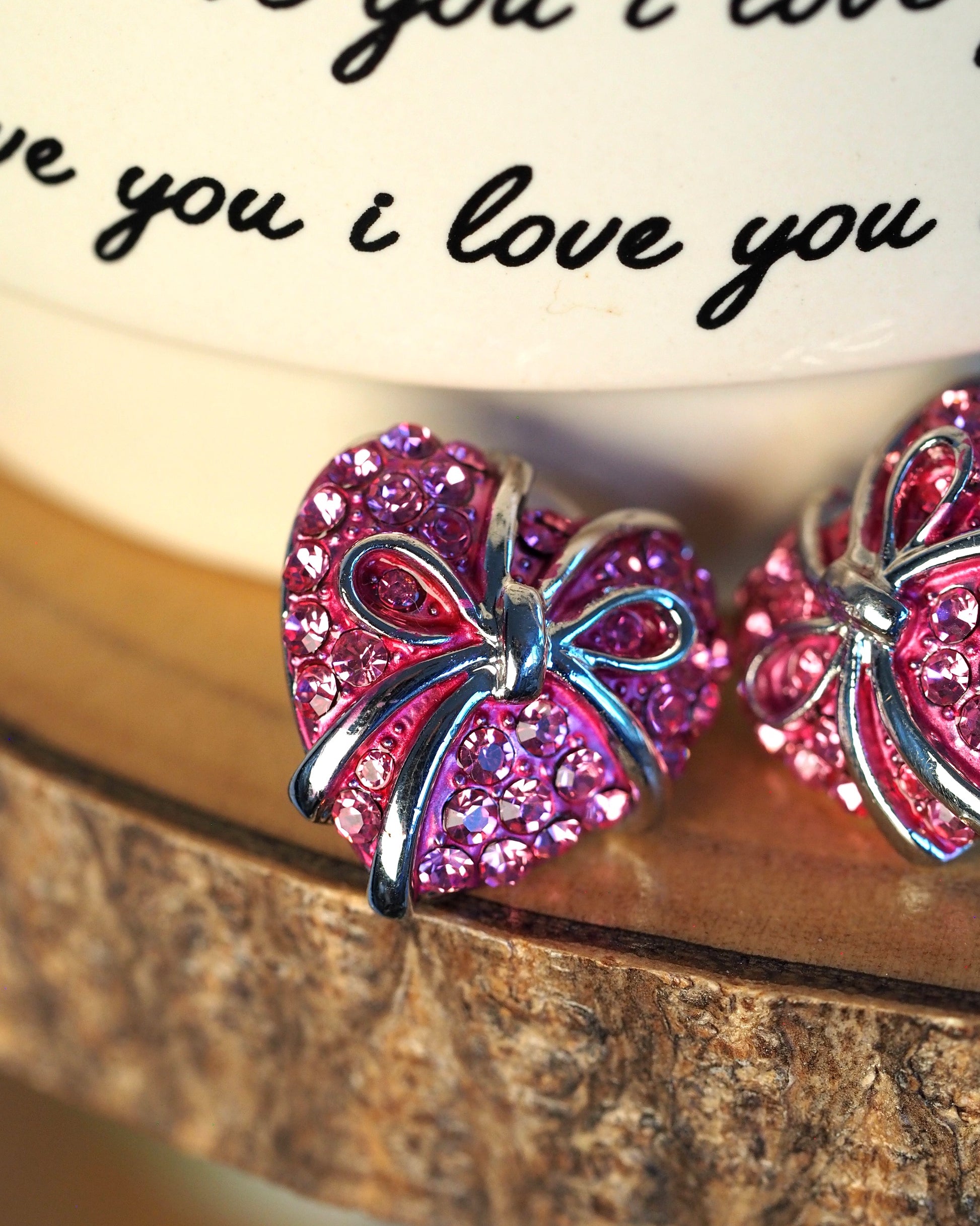 close-up of pink rhinestone heart earring with silver-tone bow detail and prong-set stones