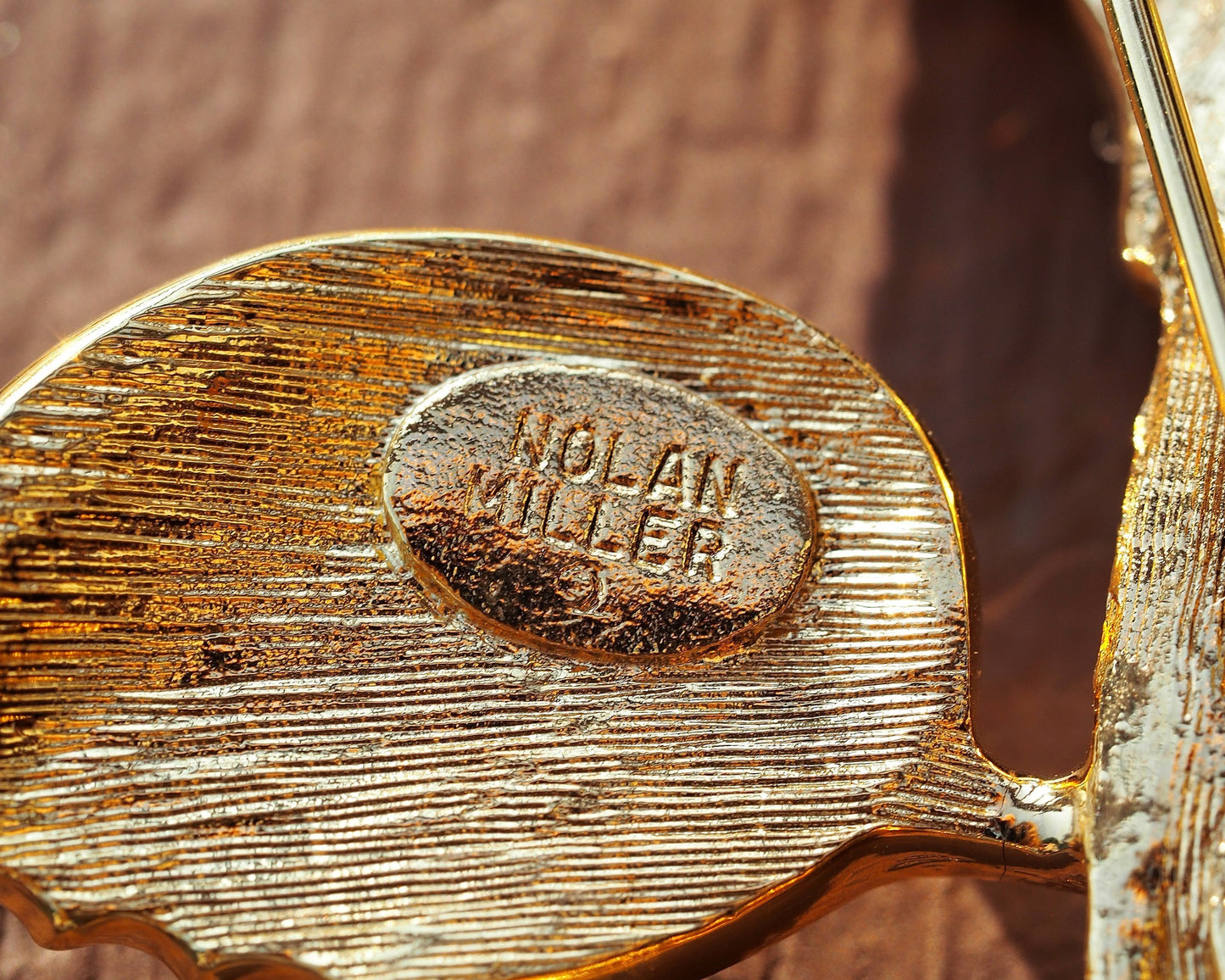 Close-up of Nolan Miller oval signature stamp on textured reverse of brooch