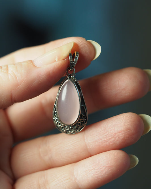 Pink glass teardrop pendant in sterling silver filigree held in palm, front view