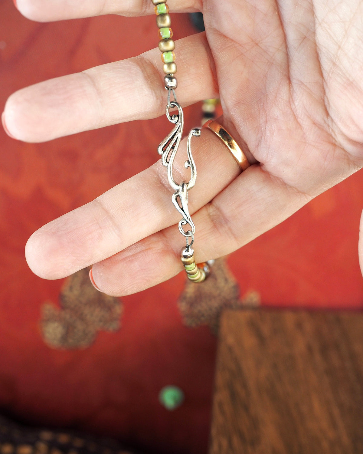 Silver-tone twisted hook clasp held in hand for scale with pale green seed beads visible