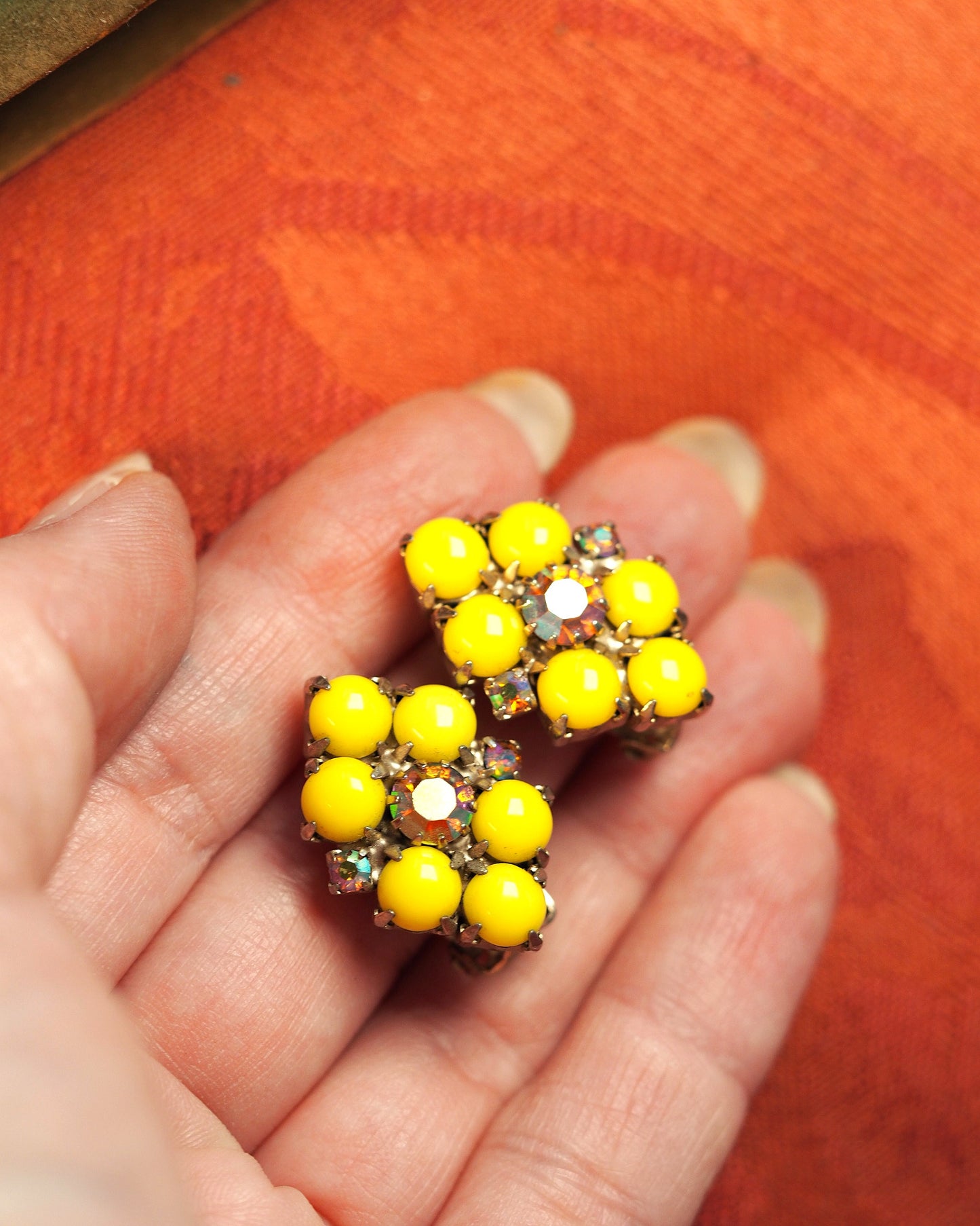 Yellow glass clip earrings shown on fingertips for scale, Aurora Borealis rhinestones sparkling at center