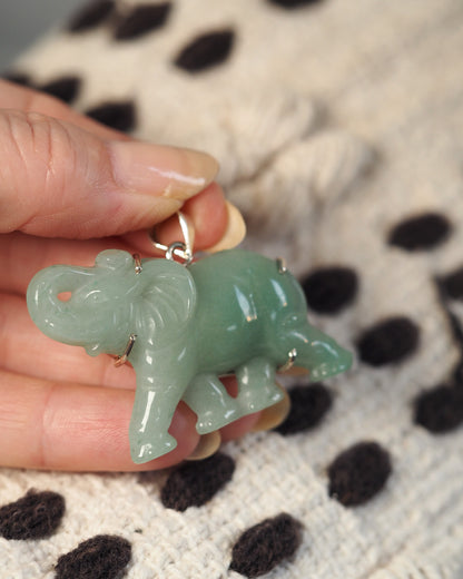 Aventurine elephant pendant held in hand for scale, showing two-inch length and translucent green stone quality