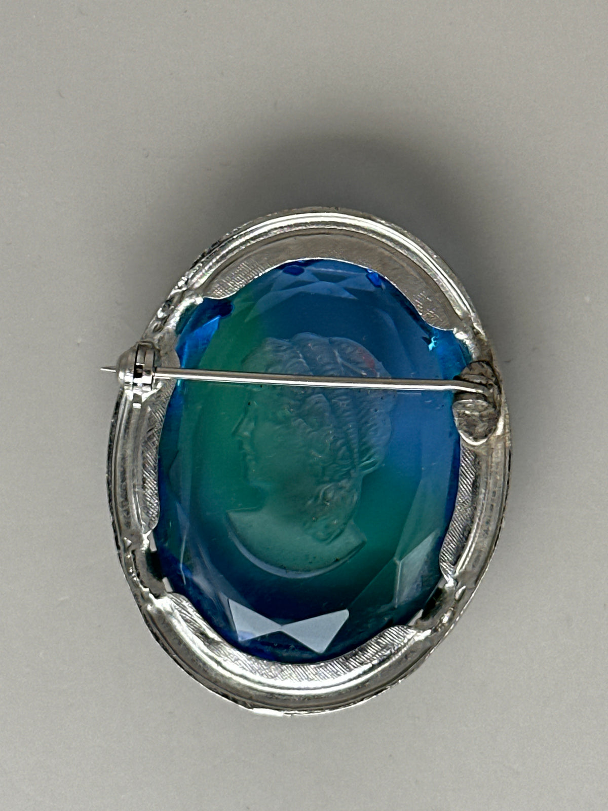 Reverse of blue glass cameo brooch showing open-back construction, C-clasp with safety catch, and engraved linear border detail
