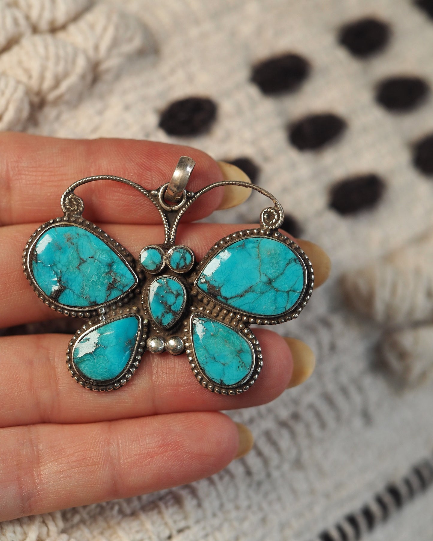 2000s reconstituted turquoise butterfly pendant held in hand for two-inch scale