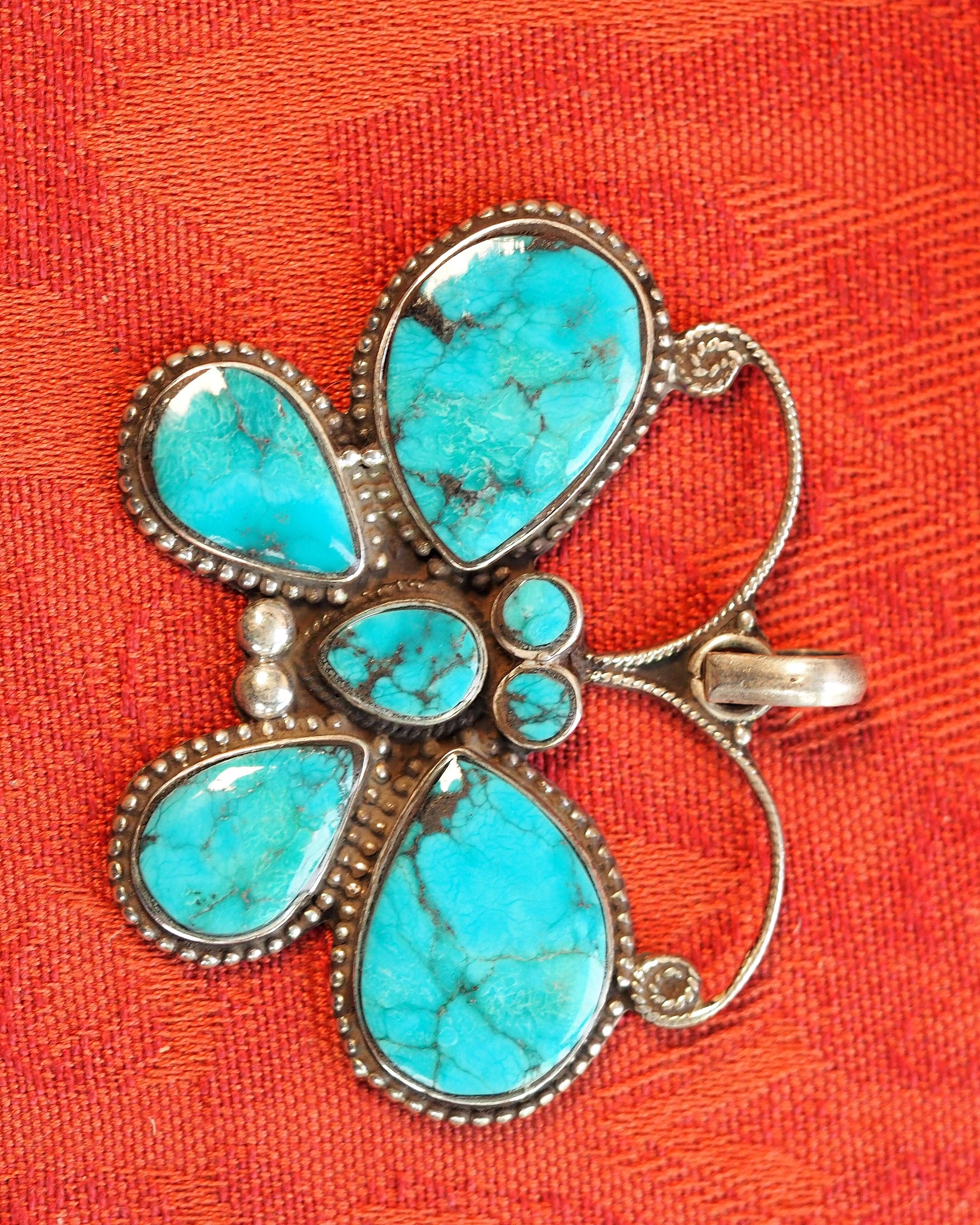 Front view of sterling silver butterfly pendant with seven turquoise cabochons on orange textile