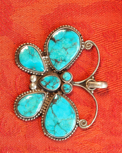 Front view of sterling silver butterfly pendant with seven turquoise cabochons on orange textile