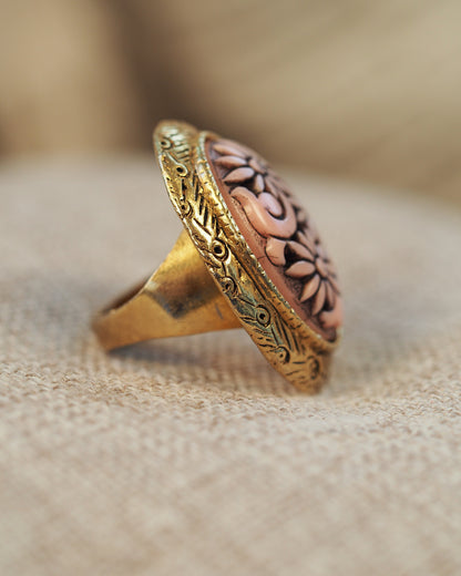 Close-up of ornate gold-tone bezel with Art Nouveau scrolls and dots surrounding pink floral cabochon