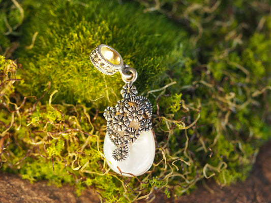 Sterling silver mother of pearl marcasite charm displayed on green moss, teardrop shape with floral cap