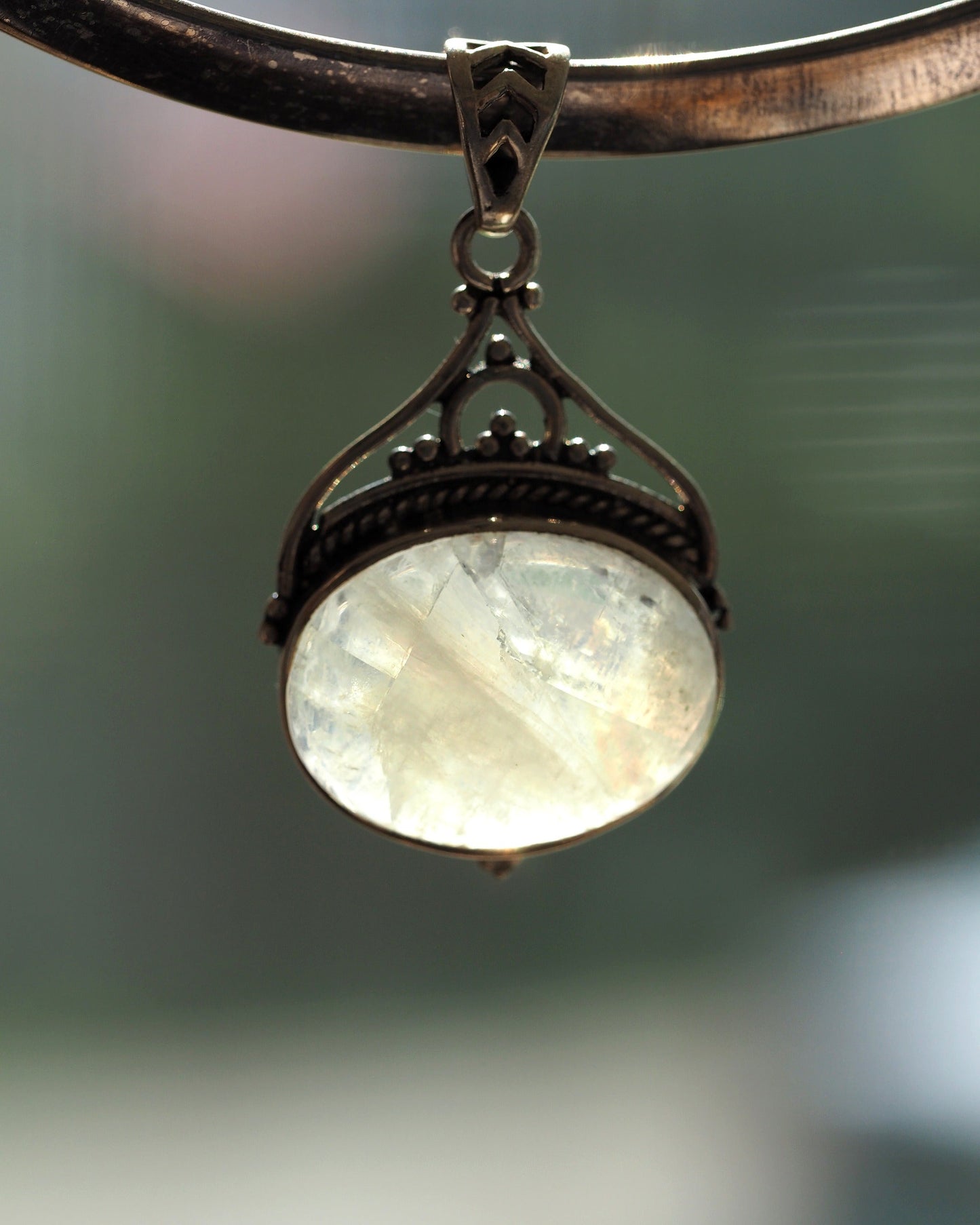 Sterling silver moonstone pendant with blue flash, filigree bail and openwork heart motif, front view on display stand