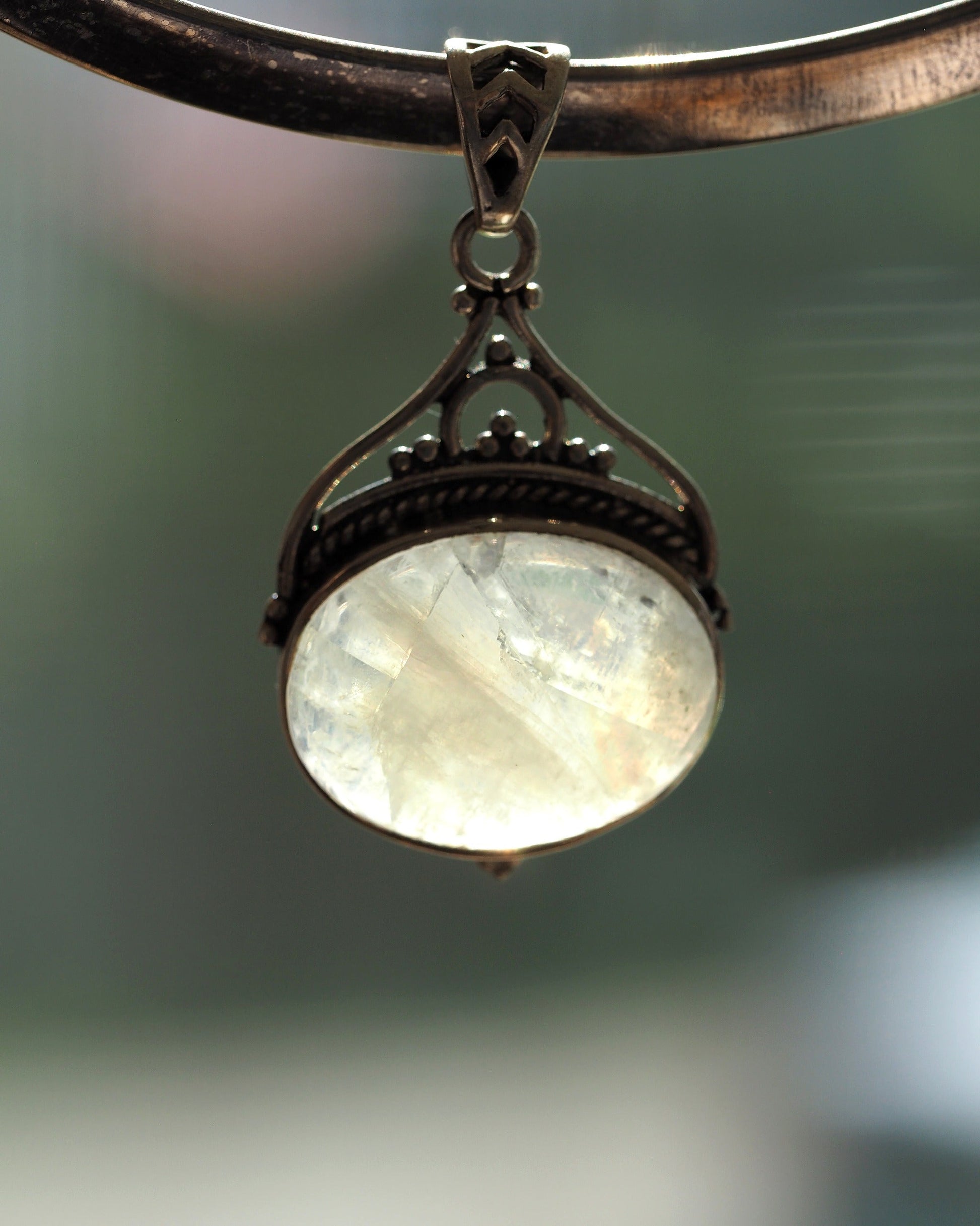 Sterling silver moonstone pendant with blue flash, filigree bail and openwork heart motif, front view on display stand