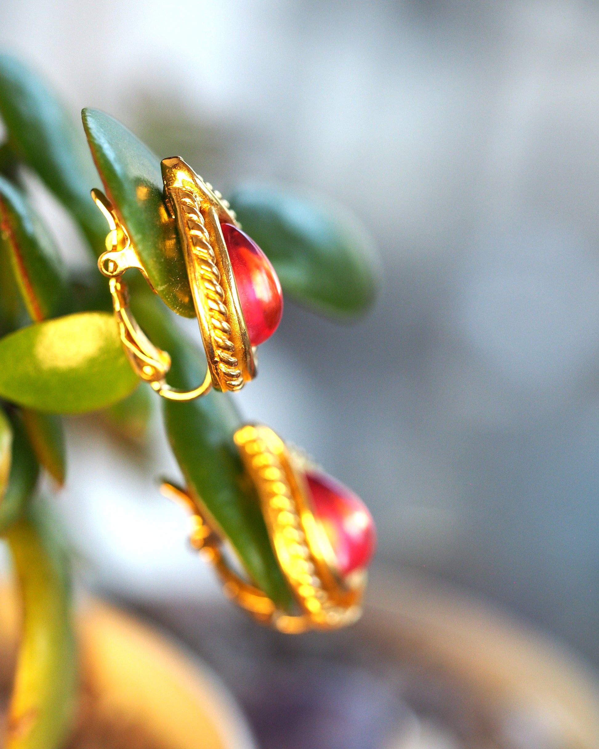 Side angle view of both Trifari clip earrings on succulent leaves, showing dimensional construction and gold finish