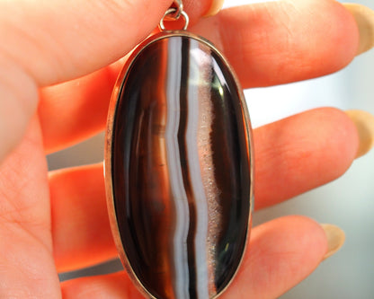 Banded agate pendant held in hand for scale, showing 2.5 inch drop and oval shape