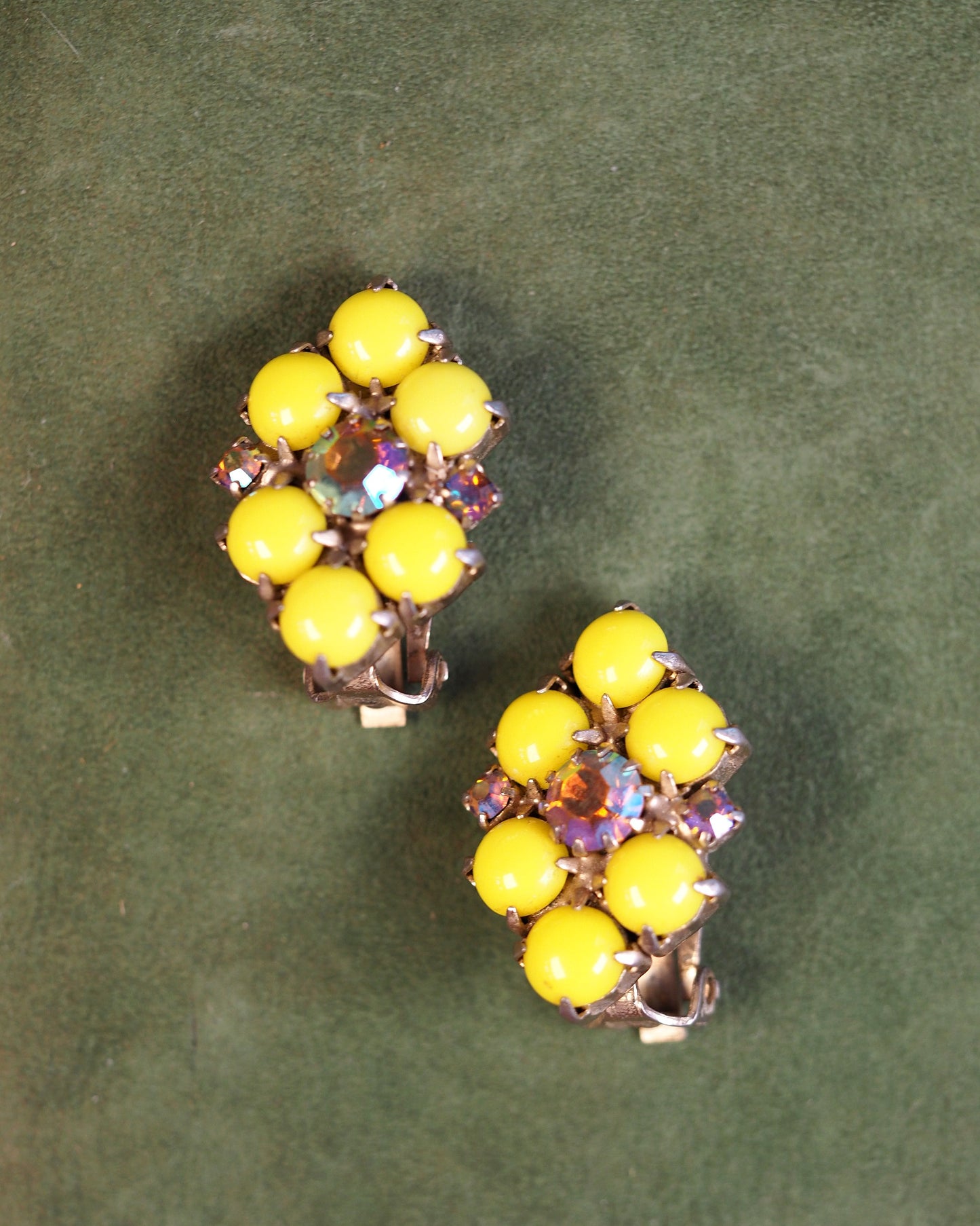Mid-Century yellow glass clip earrings with Aurora Borealis rhinestone centers, front view on green background