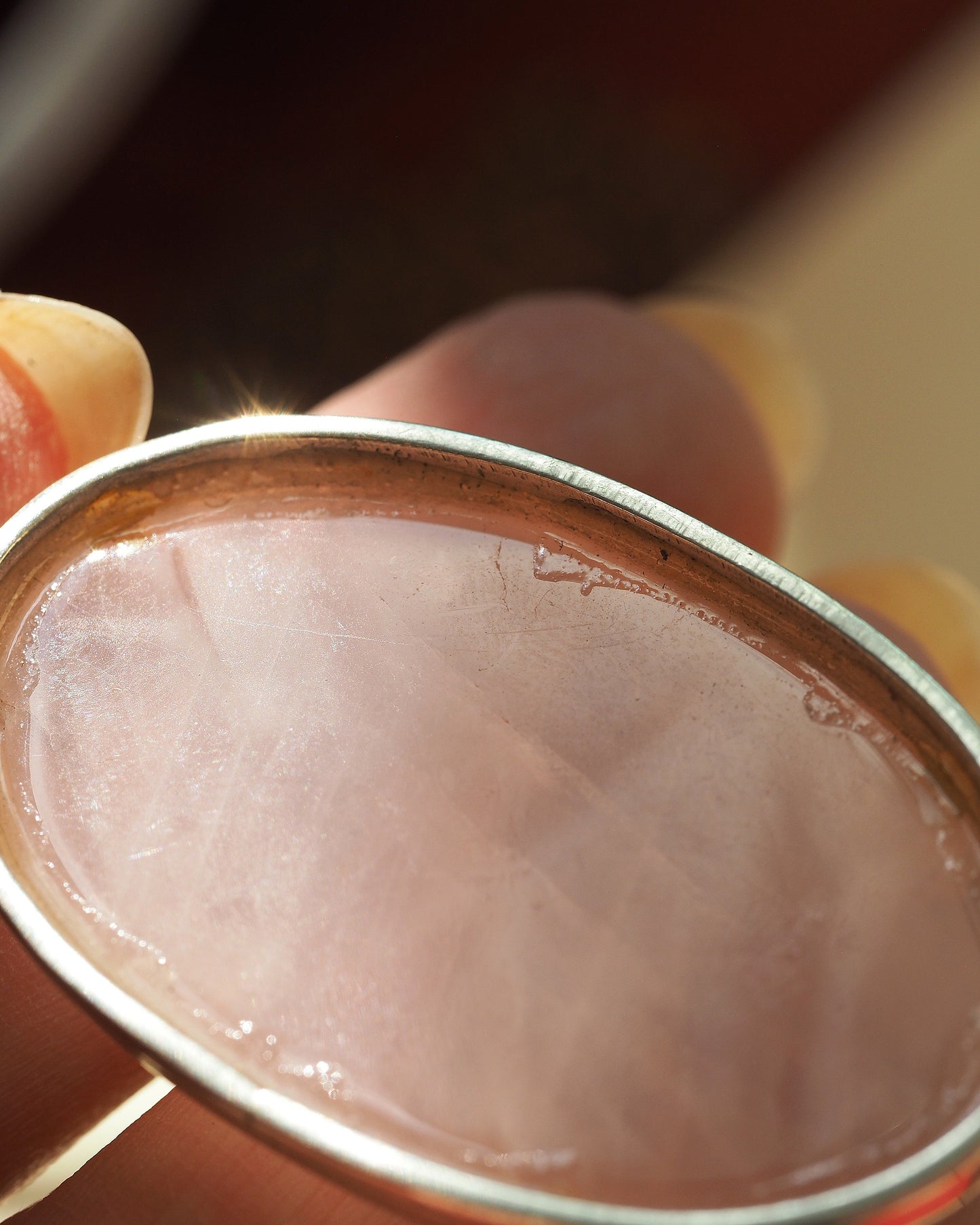 Close-up of rose quartz cabochon showing faceted surface and light surface scratches on sterling bezel rim