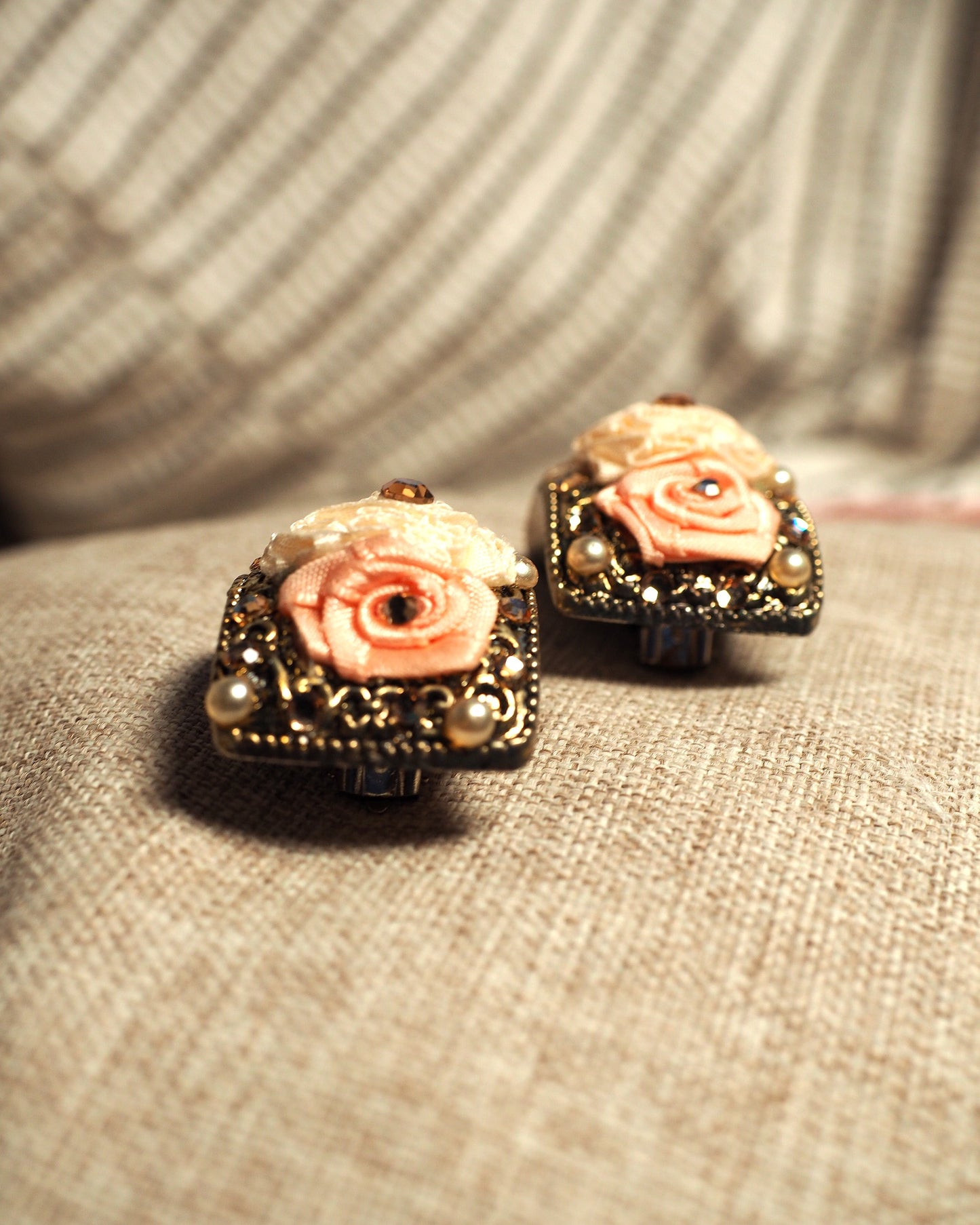 Close-up of ribbon rose clip earrings showing graduated pink tones, amber rhinestone centers, and cream faux pearls