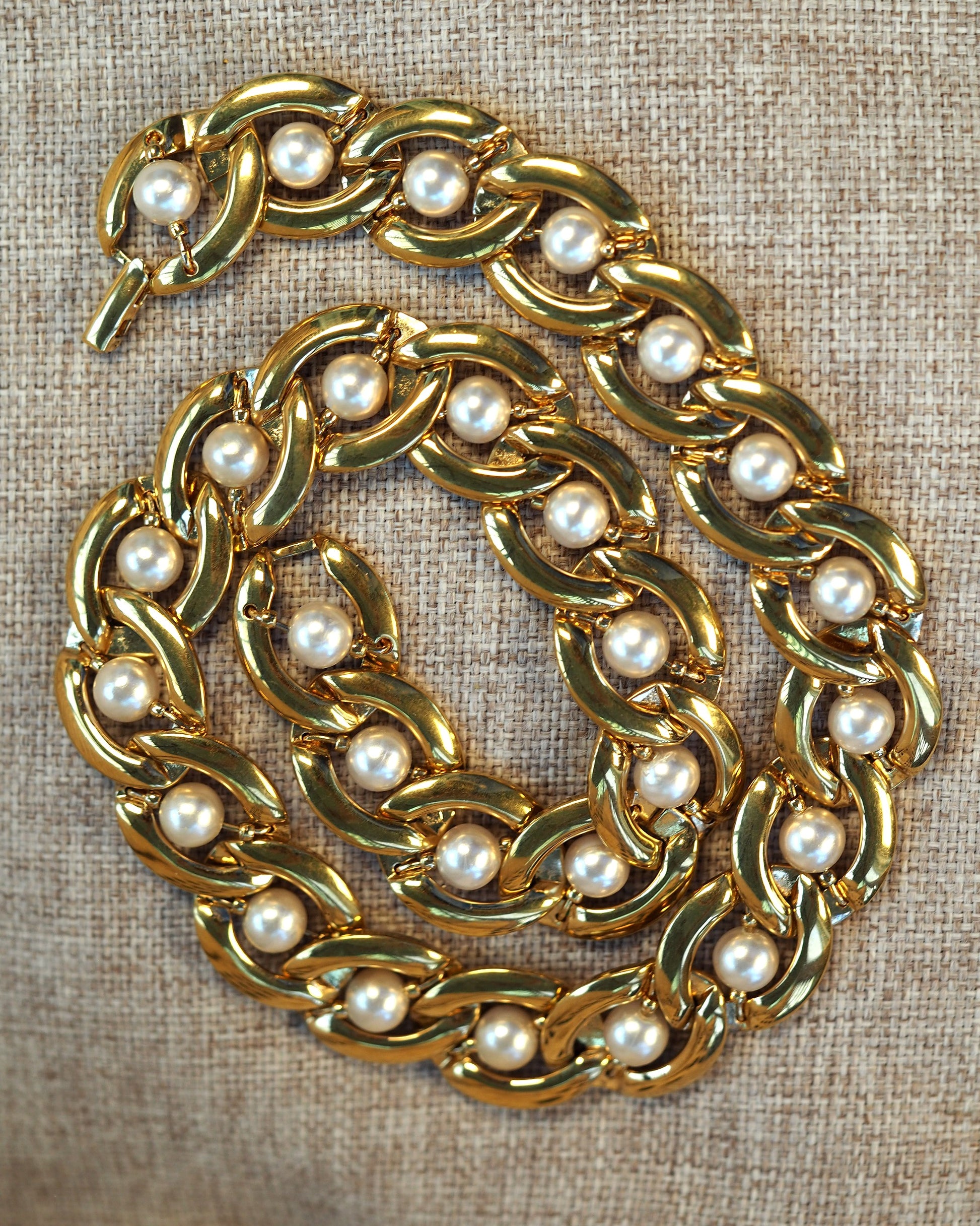 Gold-tone Napier chain necklace with faux pearl accents in each curb link, shown coiled on neutral linen