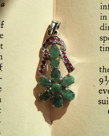 Sterling silver flower pendant with seven green cabochons and red accent stones, front view on neutral background