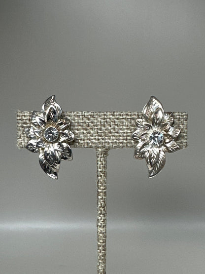Silver-tone foliate spray clip earrings with rhinestone centers displayed on earring stand, front view