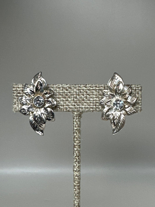 Silver-tone foliate spray clip earrings with rhinestone centers displayed on earring stand, front view