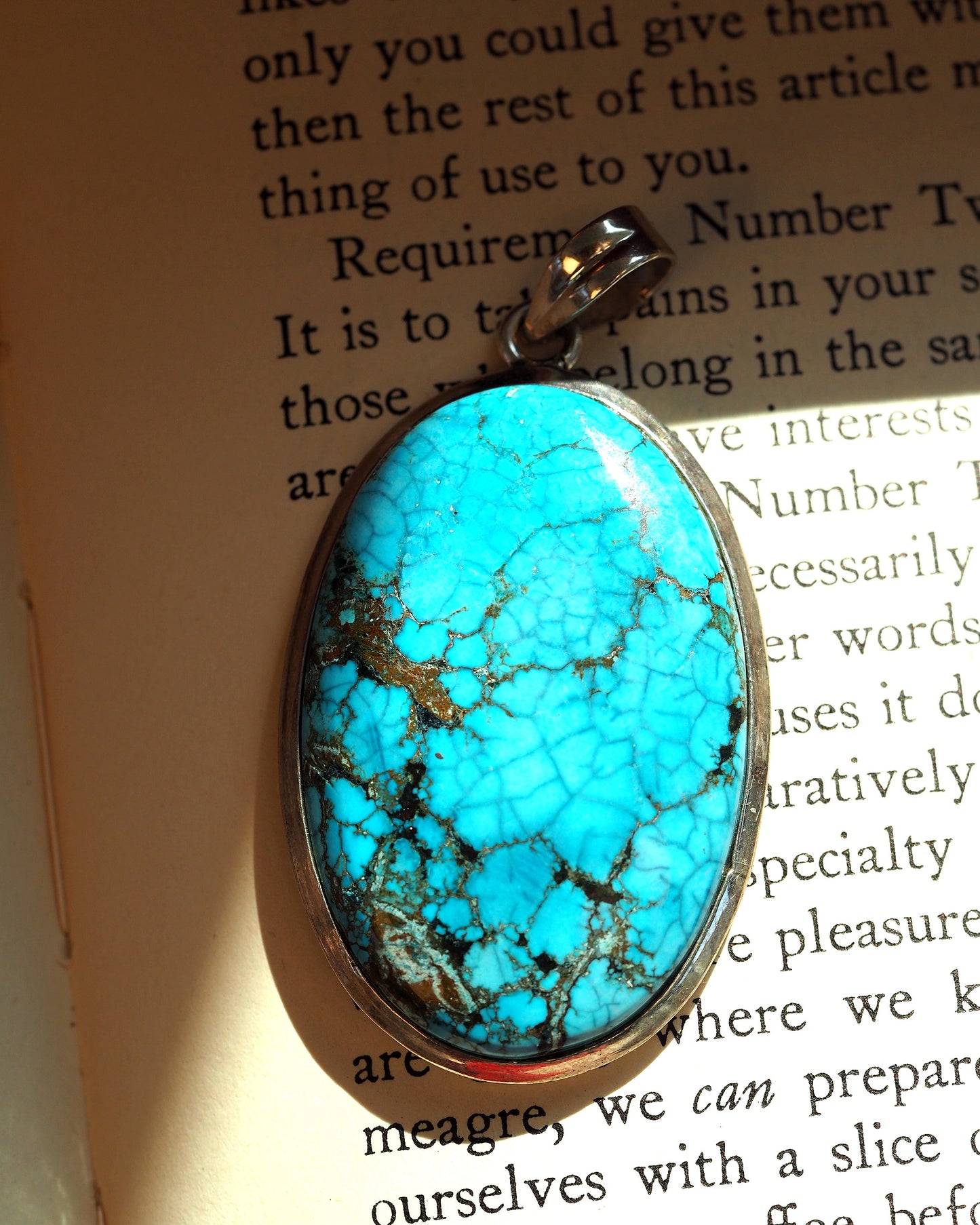 Close-up of turquoise cabochon with bright blue color and brown spiderweb matrix in bezel setting