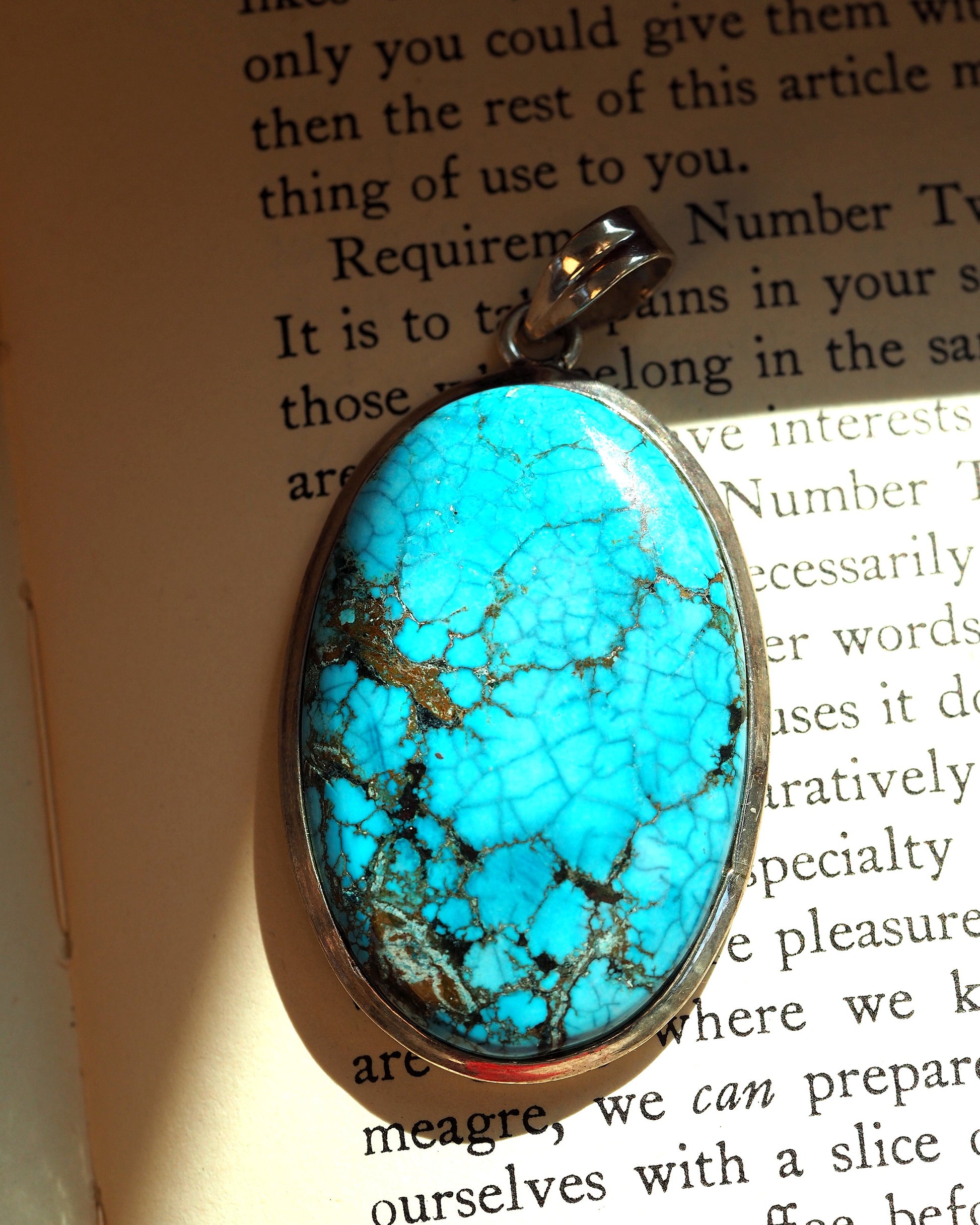 Close-up of turquoise cabochon with bright blue color and brown spiderweb matrix in bezel setting