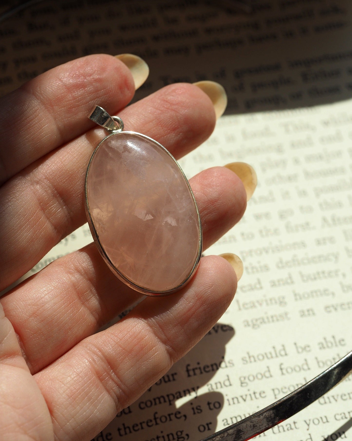 rose quartz pendant held on fingertips for scale, showing size relative to hand
