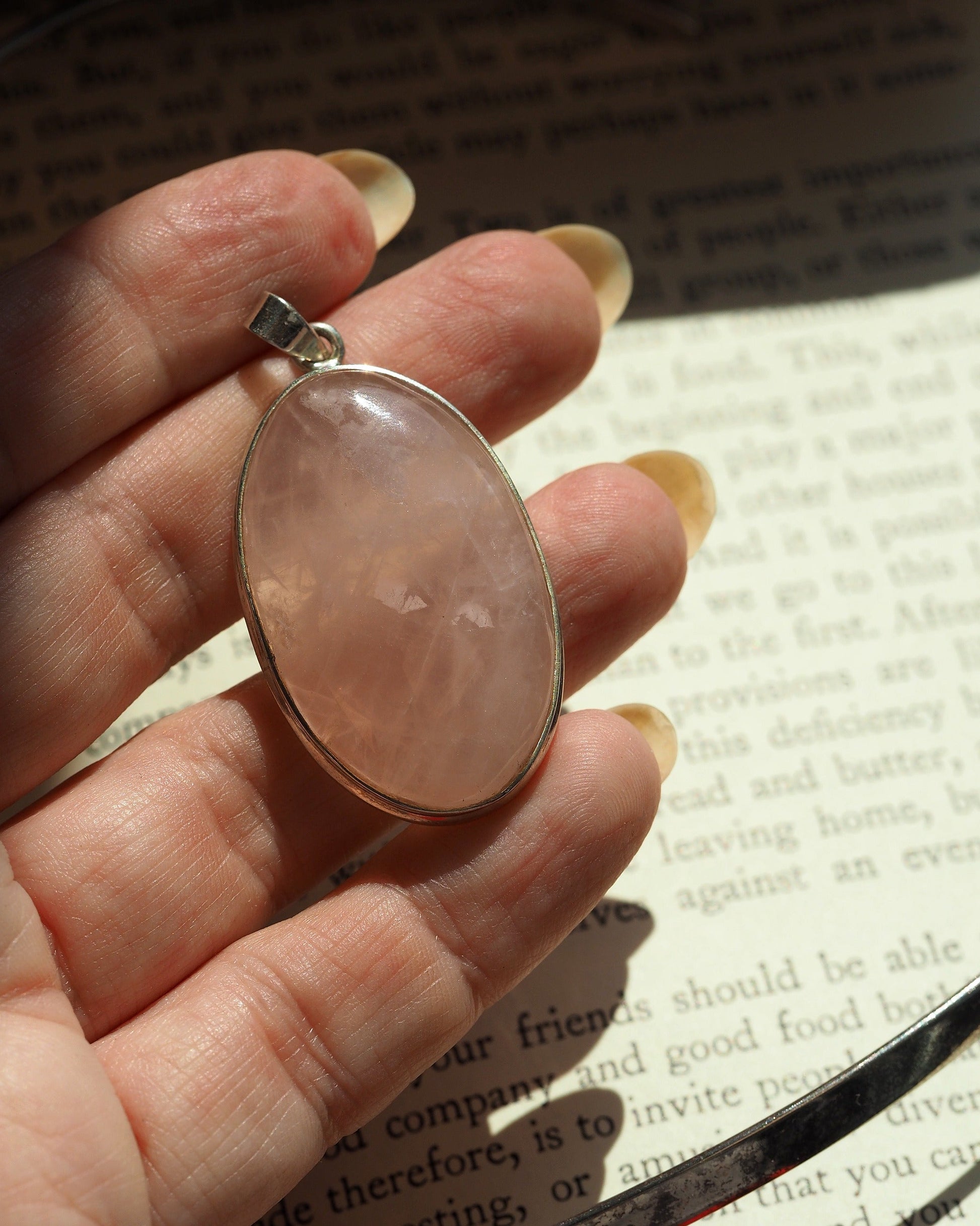 rose quartz pendant held on fingertips for scale, showing size relative to hand