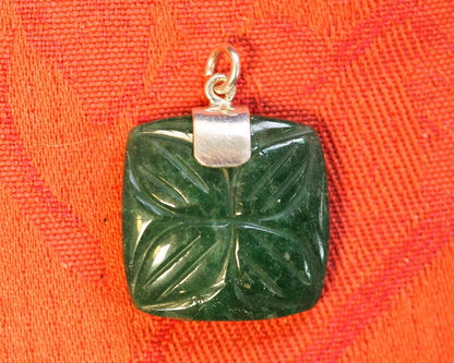 2000s aventurine pendant on orange linen, showing the square carved stone with symmetrical floral motif and silver cap