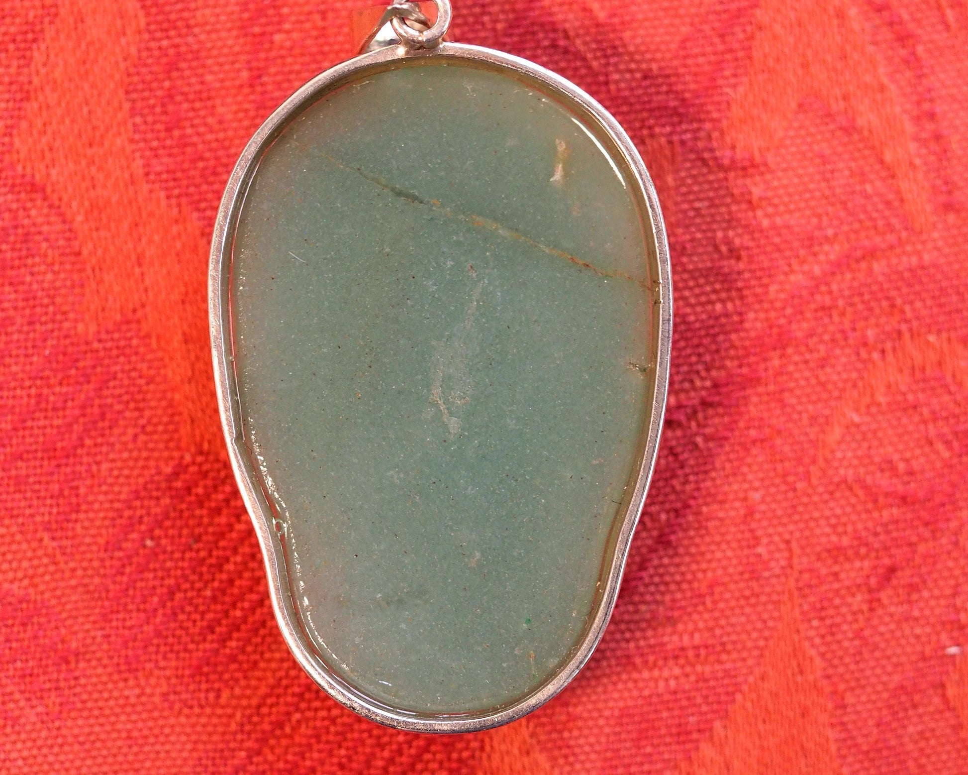 Back of aventurine skull pendant showing smooth polished stone reverse and sterling silver bezel, natural color variations visible