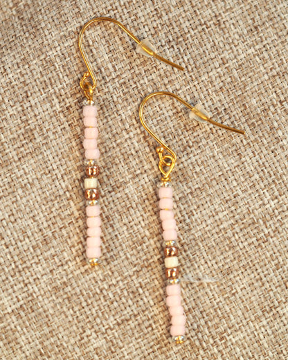 Pink Japanese glass bead drop earrings with gold-tone spacers on fishhook ear wires, shown flat on woven textile background